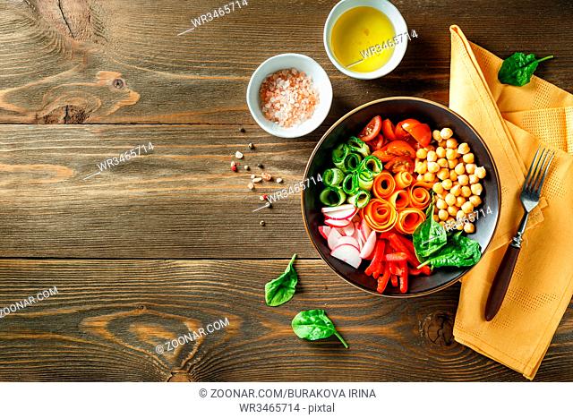 Colorful Buddha Bowl with chickpeas, carrots, tomatoes, cucumbers, radish and peppers on a wooden table. Vegetarian salad. Top view. Space for text