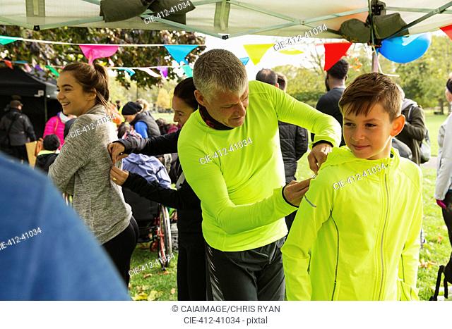 Father pinning marathon bib on son at charity run in park tent