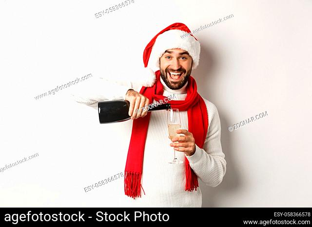 Christmas party and holidays concept. Happy bearded man in Santa hat and scard, pour himself champagne and smiling, celebrating New Year