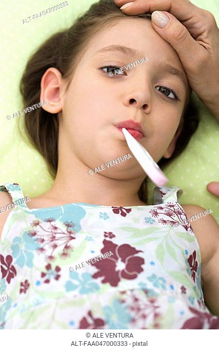 Little girl lying down with thermometer in mouth