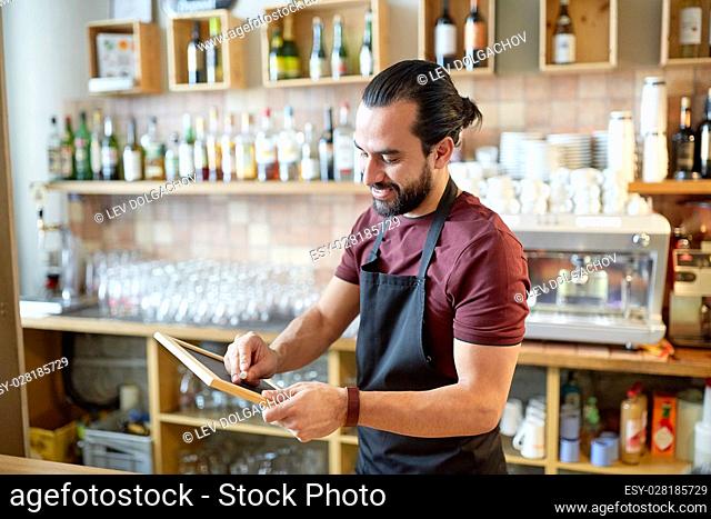 small business, people and service concept - happy man or waiter in apron with black chalkboard banner at bar or coffee shop