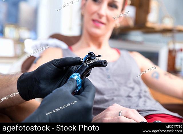 Close-up of the hands of a tattoo artist wearing black sterile gloves while preparing a professional machine for tattooing a female client