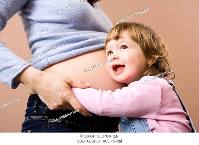 Girl listening at pregnant mothers belly