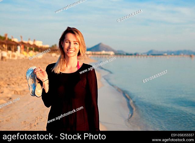 Cheerful blond woman walking along tropical sea beach at sunset