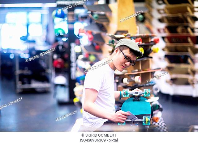 Young male sales assistant repairing skateboard at skateboard shop counter
