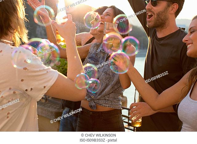 Adult friends playing with floating bubbles at roof terrace party