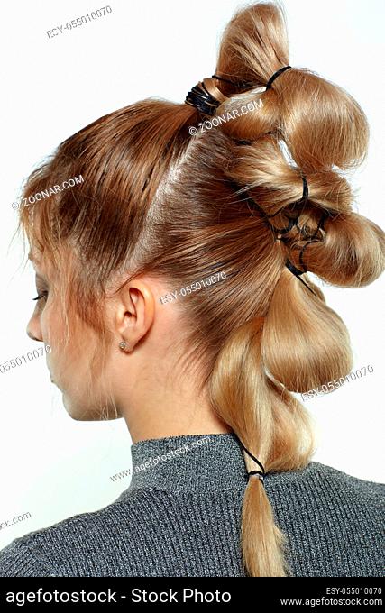 Back view portrait of beautiful young dark blonde woman. Female with creative braid hairdo on gray background