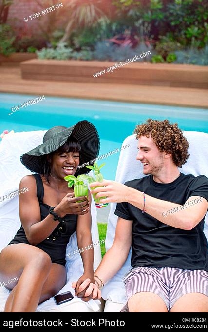 Happy young multiethnic couple drinking cocktails at poolside