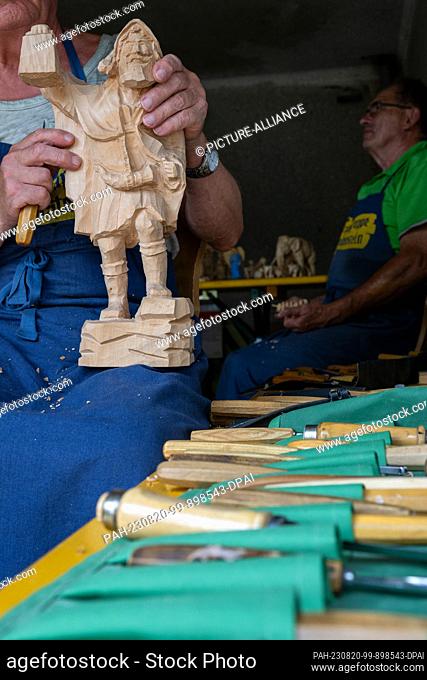 20 August 2023, Bavaria, Hallerstein: A woodcarver makes the final touches to a figurine. Nearly 60 regional and almost forgotten crafts were presented at the...