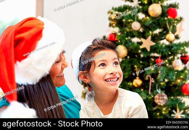 happy mother and little girl in santa hats at home