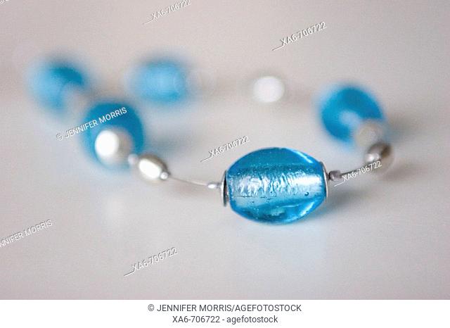 A necklace consisting of large blue glass beads on a silver wire. One bead is in focus in the foreground and the rest fall out of focus on the light grey...