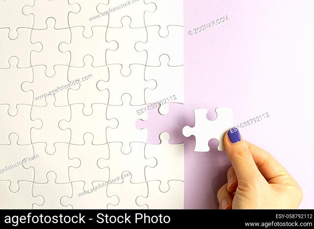 Set of white puzzle pieces and hand holding last one piece on purple background. top view