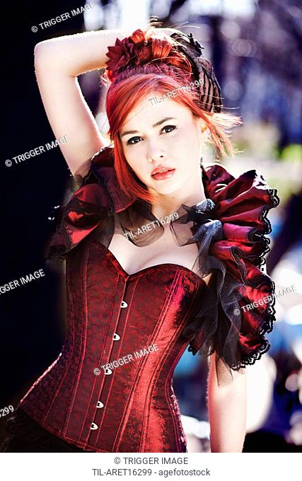 Young female with arm up looking into the camera wearing a sexy red corset