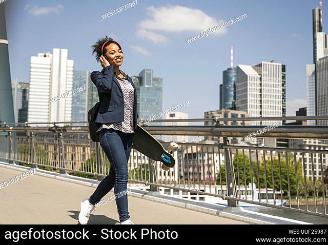 Businesswoman with skateboard walking on bridge
