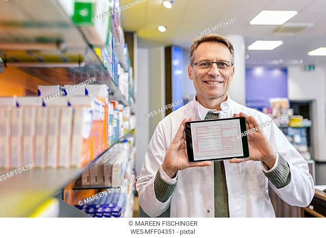 Portrait of smiling pharmacist in pharmacy holding tablet with digital prescription