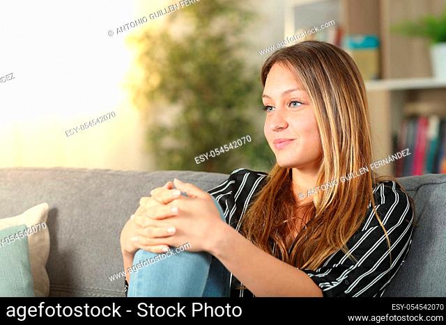 Satisfied homeowner thinking looking away sitting on a couch at home