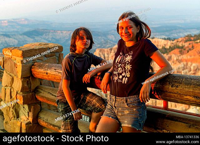 Girl and boy enjoying the sunset from Rainbow Point - a National park peak with red & pink cliffs & rock formations, spruce & fir forest & hiking trails