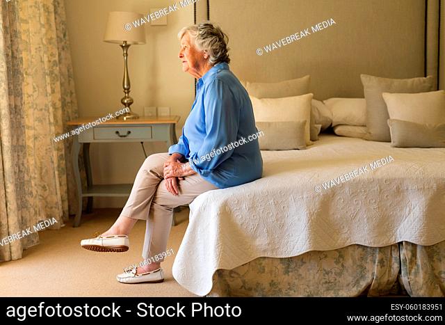 Senior caucasian woman sitting on bed and thinking in bedroom