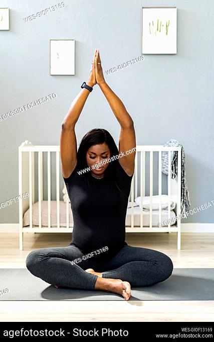 Young pregnant woman with arms raised practicing yoga at home