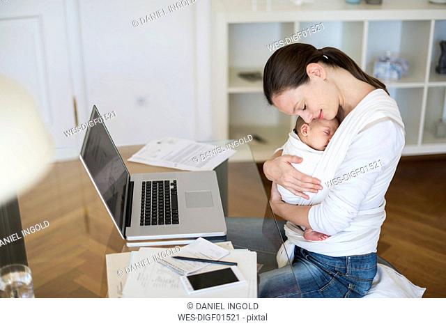 Mother with baby girl in sling working from home