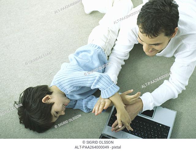 Man and little boy lying on floor with laptop playing