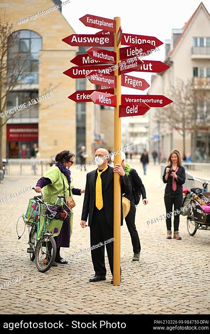 26 March 2021, Saxony-Anhalt, Halberstadt: Action artist Thomas Peters from Quedlinburg stands on the market square in Halberstadt and carries a sign tree on...