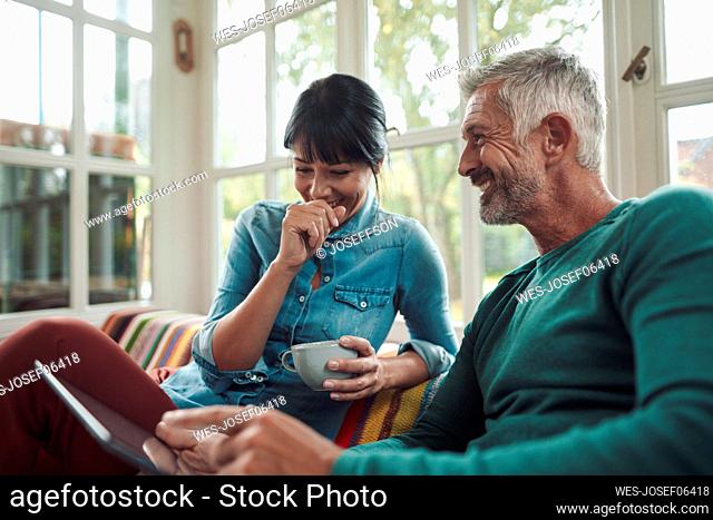 Smiling man talking with woman holding coffee cup at home