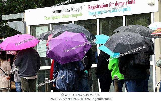 People carrying umbrellas stand in line to register to enter the Reichstag building under pouring rain and temperatures of 16 degreees Celsius in Berlin
