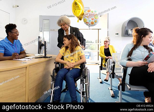 Female receptionist greeting girl patient in wheelchair in clinic