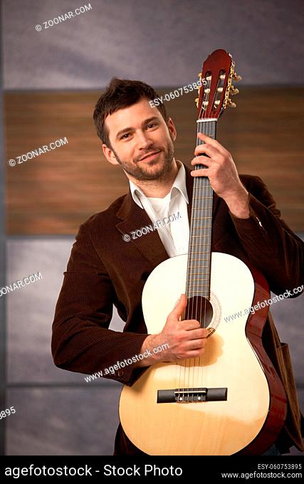 Handsome stylish guy standing holding guitar, smiling at camera