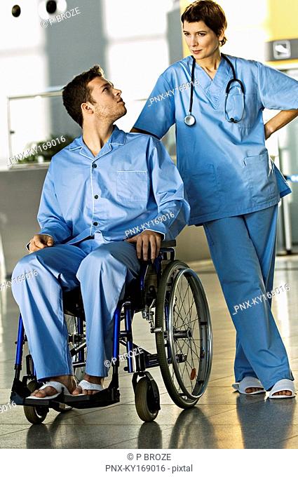 Male patient sitting in a wheelchair and looking at a female doctor standing beside him