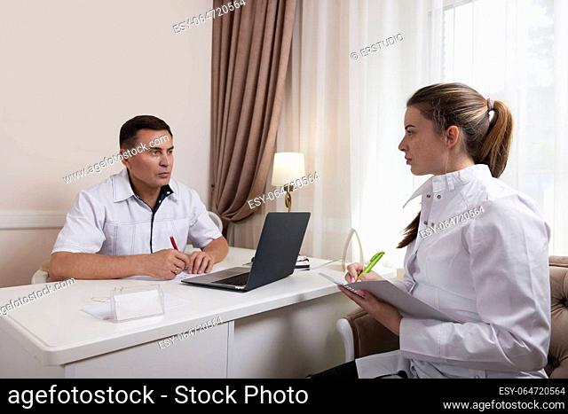 Two doctors man and woman talking, looking at computer screen, analyzing results of patients medical examination at workplace