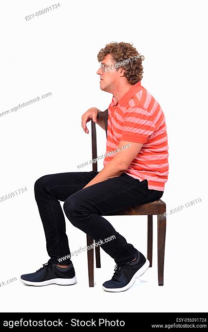 full portrait of a curly man sitting sideways on white background,