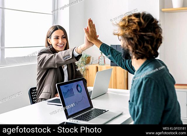 Smiling young businesswoman giving high-five to colleague at desk