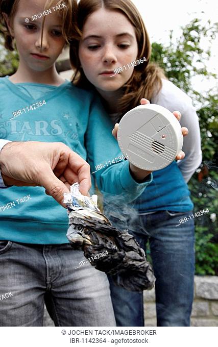 A father demonstrating to his daughters the function of a smoke detector with the help of a burning, fuming piece of paper, in the garden, Germany, Europe