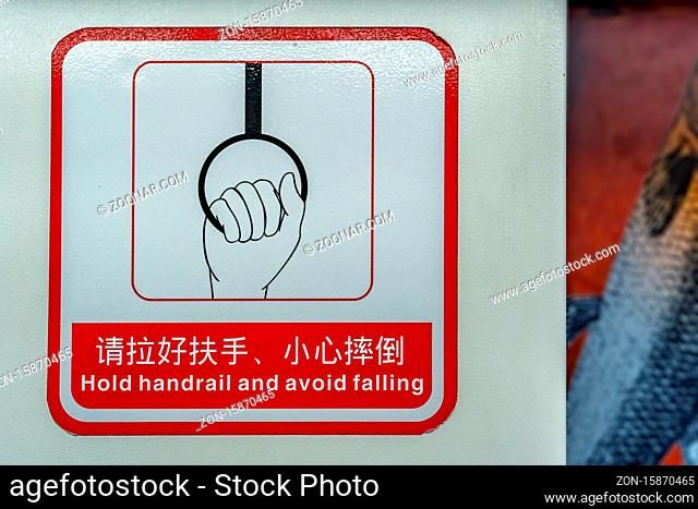 Chongqing, China - August 2019 : Red and white warning sign in English and chinese characters spelling Hold handrail and avoid falling inside a underground...