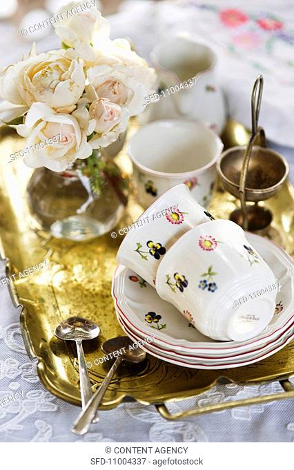 Crockery and a bunch of flowers on a golden tray