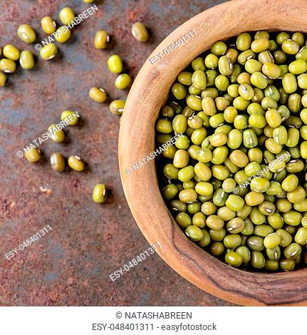 Healthy superfood. Uncooked green mungo beans in olive wood bowl over old rusty iron background. Top view. Close up. Square image