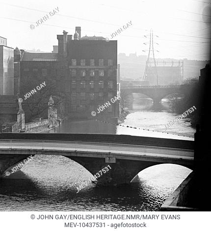 Looking along an industrialised river with two arched bridges visible further along the watercourse. Possibly Huddersfield., West Yorkshire