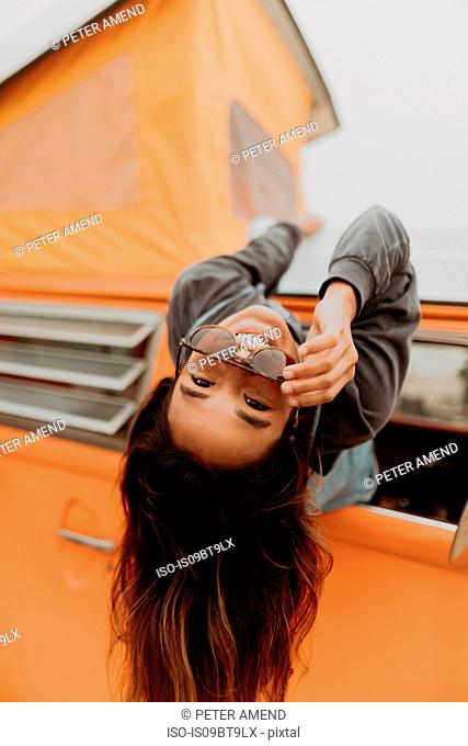 Young woman hanging out of recreational vehicle window at beach, portrait, Jalama, California, USA