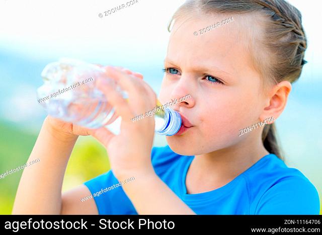 little girl drinking fresh water from bottle on light nature background