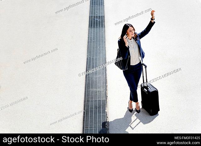 Businesswoman with suitcase hailing ride during sunny day