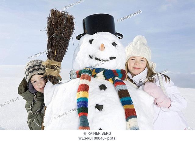 Germany, Bavaria, Munich, Boy 8-9 and girl 8-9 standing next to snowman, portrait