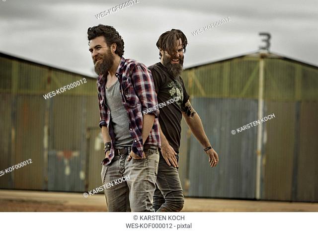 Two smiling men with full beards in abandoned landscape