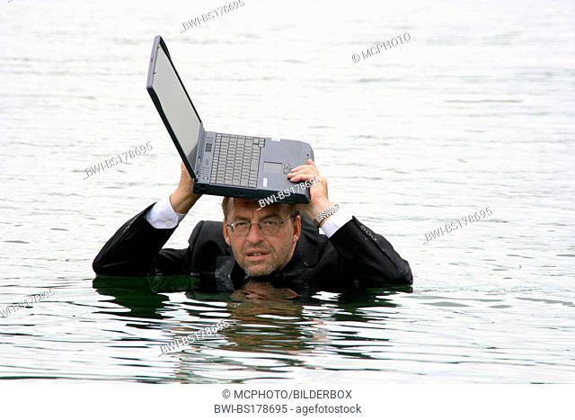 businessman in deep water holdig laptop over his head
