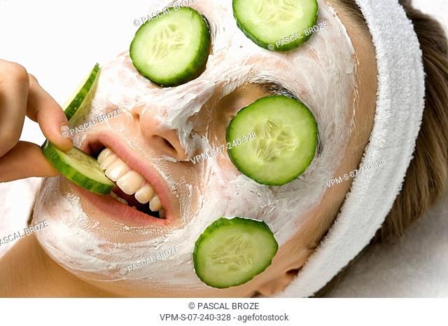Close-up of a young woman with a facial mask and cucumber slices on her eyes