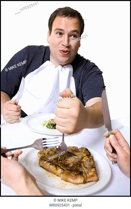 Overweight man stealing steak off partners plate
