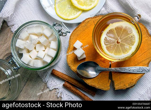 Glass transparent cup with mint tea stands on a wooden stand, next to a sugar bowl with sugar cubes, sliced lemon and a spoon