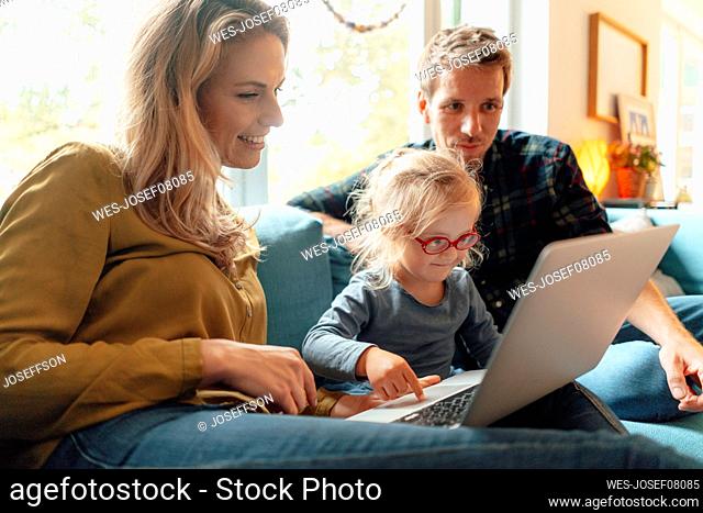 Little girl using laptop sitting with parents on sofa at home