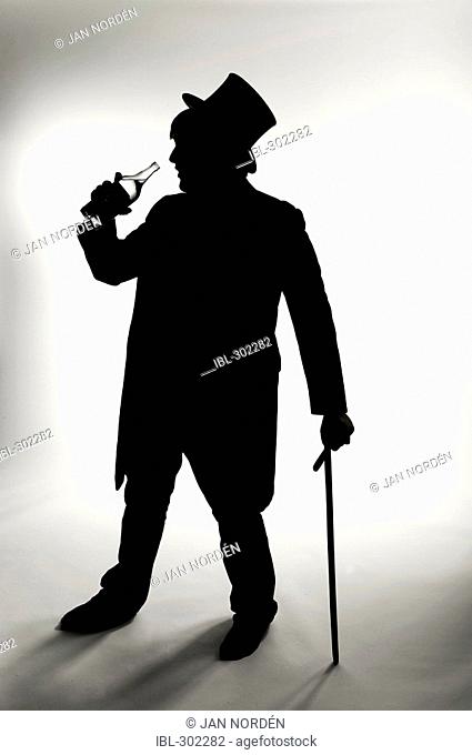 Silhouette of man with hat and stick, drinking from a bottle